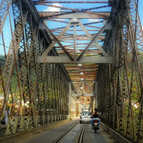 Interior da Ponte Dom Pedro II, com a estrutura metálica, os trilhos e um carro atravessando