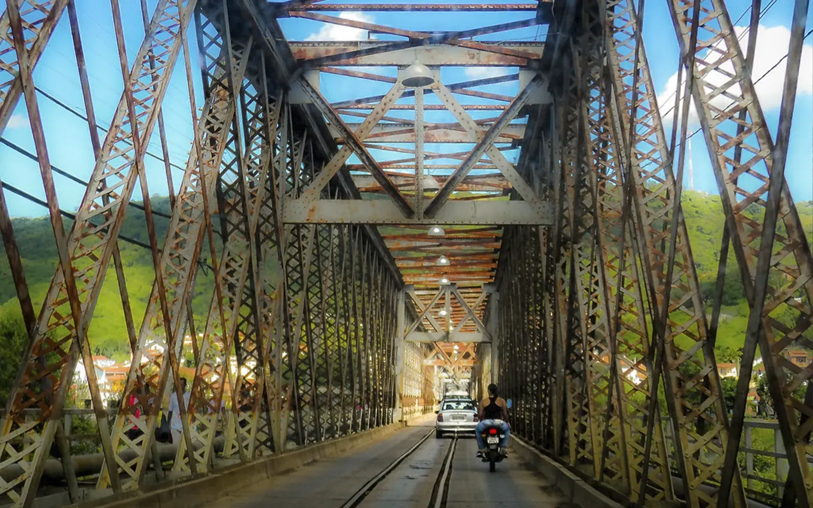 Interior da Ponte Dom Pedro II, com a estrutura metálica, os trilhos e um carro atravessando