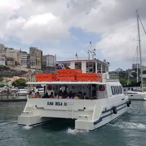 Catamarã Ilha Bela III com passageiros no salão aberto, saindo de Salvador com a Cidade Alta ao fundo