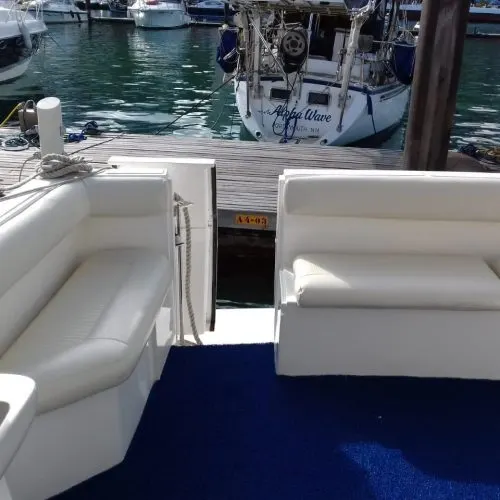Bancos estofados na popa da lancha, com a plataforma de embarque e a marina ao fundo