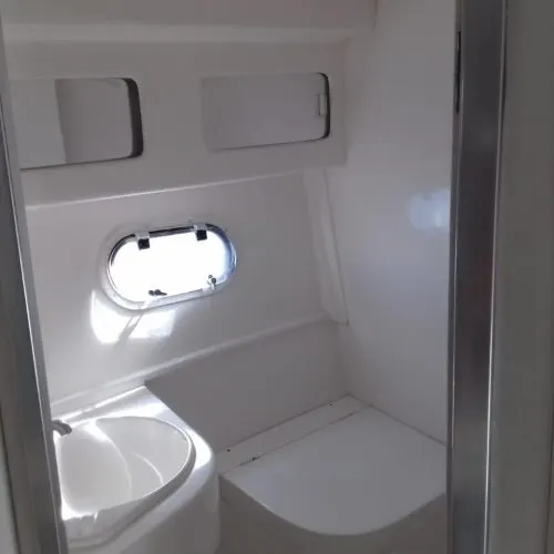 Banheiro interno da lancha, com pia, vaso e escotilha