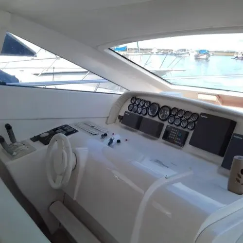 Cabine de comando da lancha, com volante, mostradores e vista para a marina