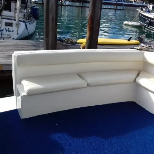 Sofá branco na popa da lancha, sobre o carpete azul, com a marina ao fundo