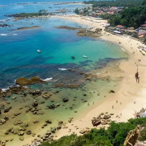 Enseada de Morro de São Paulo com recifes rasos, lanchas fundeadas e guarda-sóis na areia