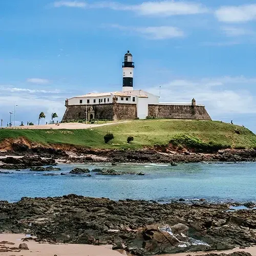Farol da Barra sobre o Forte de Santo Antônio, com as pedras e o mar da praia em primeiro plano